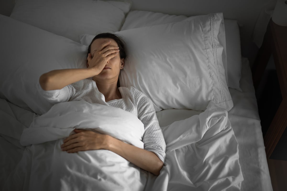 A person resting in bed at home, visibly tired and uncomfortable