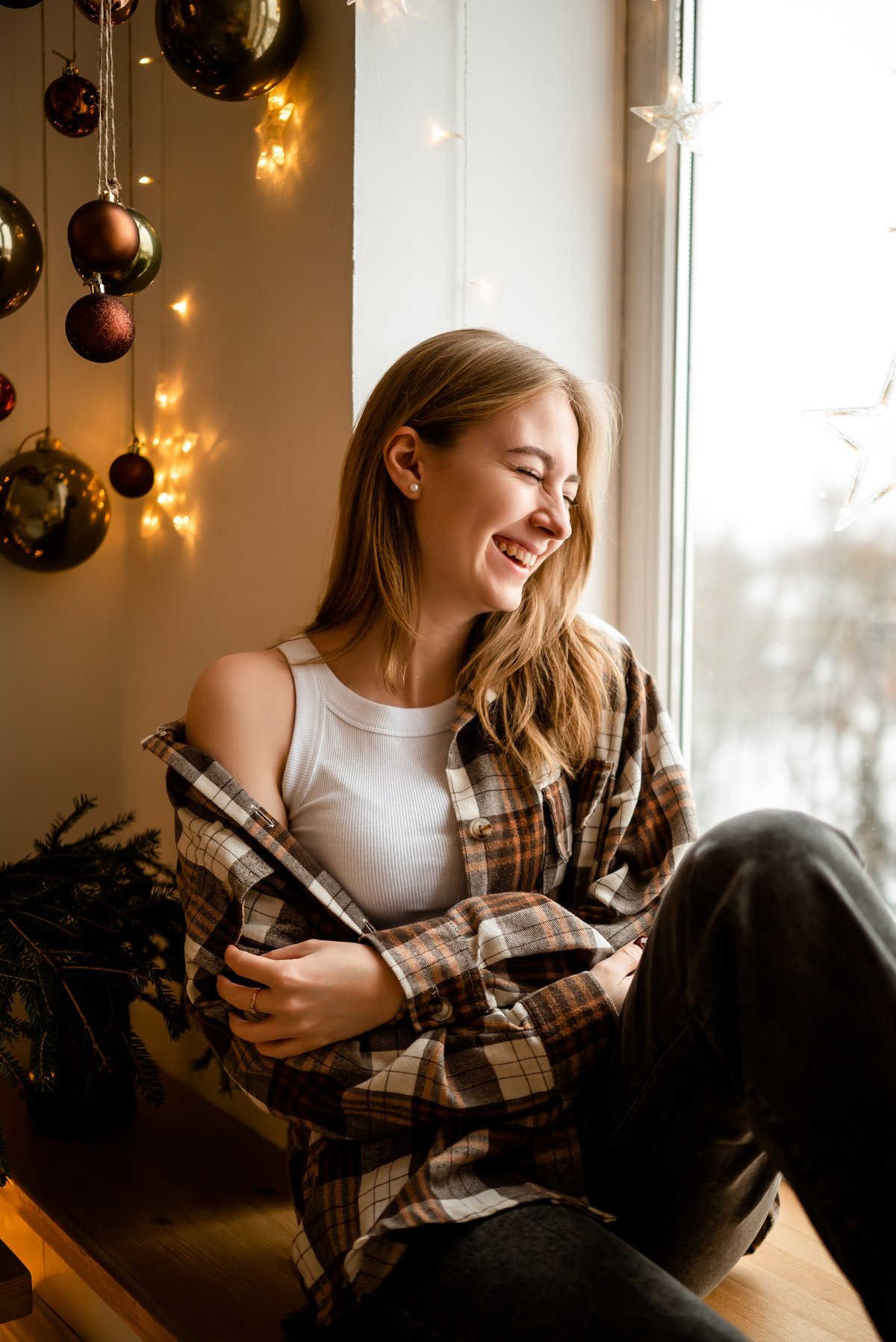 A person sitting by a window at home, wrapped in a warm shirt, looking calm